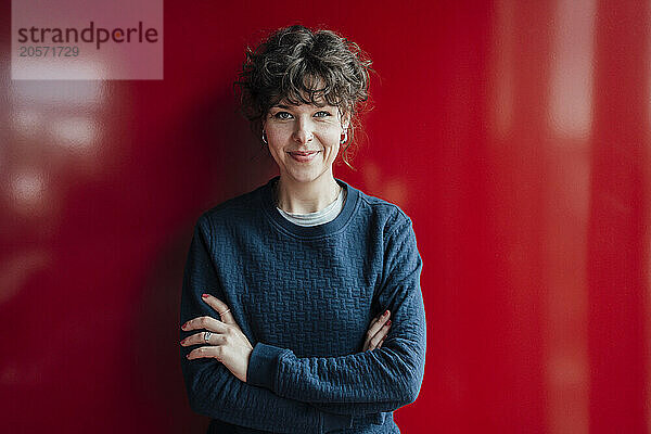 Smiling entrepreneur with smart phone in front of red wall