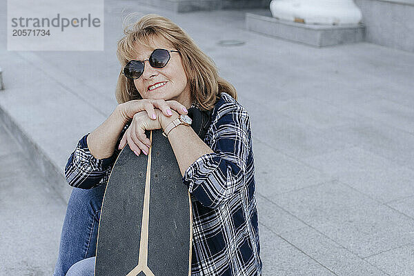 Smiling senior woman leaning on skateboard in park