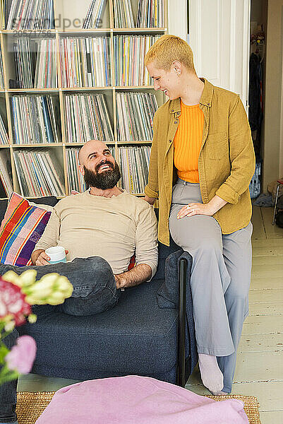 Smiling man talking with woman sitting on sofa at home