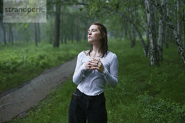 Thoughtful woman standing in rain at forest