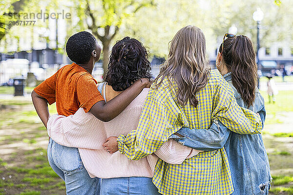 Multiracial women standing with arms around each other at park