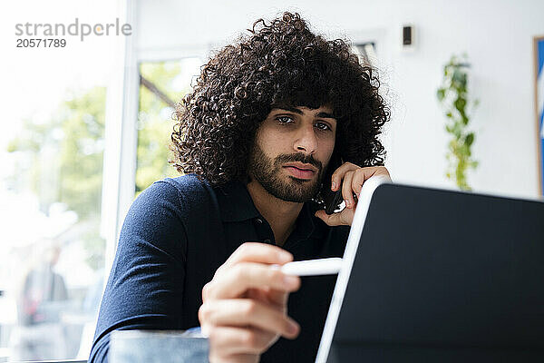 Confident businessman talking on mobile phone and using tablet PC at office