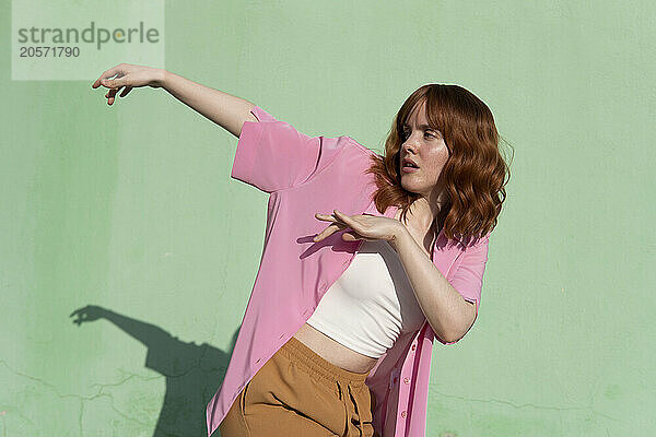 Confident redhead woman dancing with in front of mint green wall on sunny day