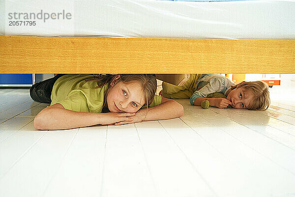 Playful siblings hiding under bed at home