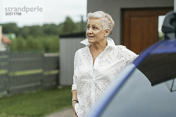 Confident senior woman near electric car