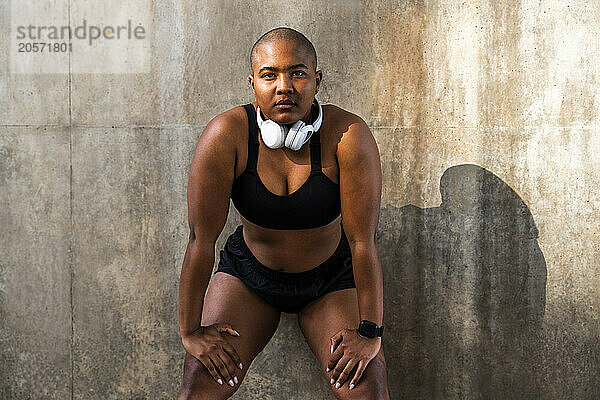 Exhausted sporty woman with hand on knees in front of wall