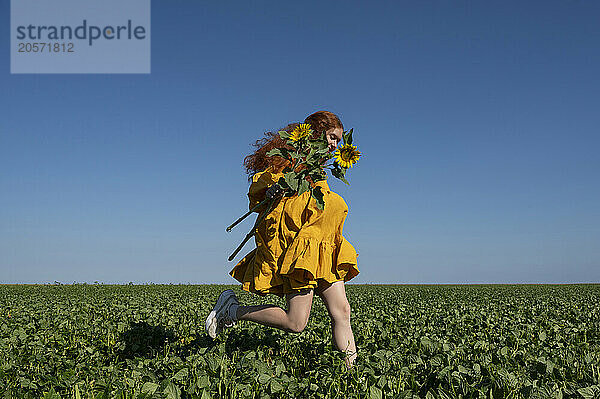 Teenage girl with red hair in a yellow dress running with sunflowers in a green field