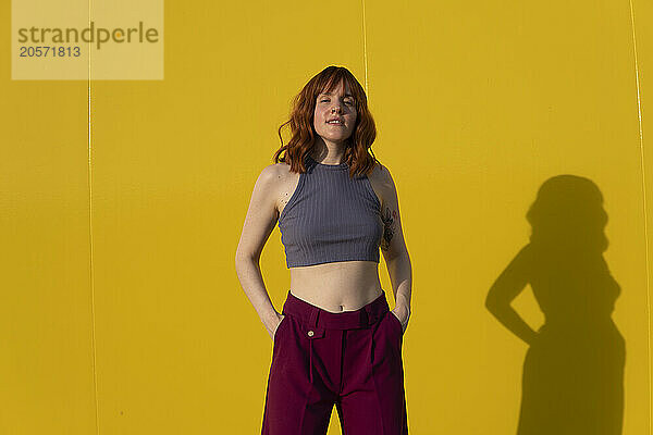 Confident redhead woman standing in front of yellow wall