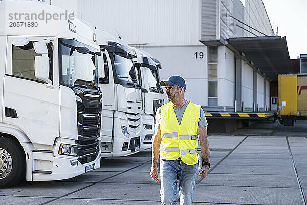 Confident mature manager wearing reflective workwear walking with tablet PC outside warehouse