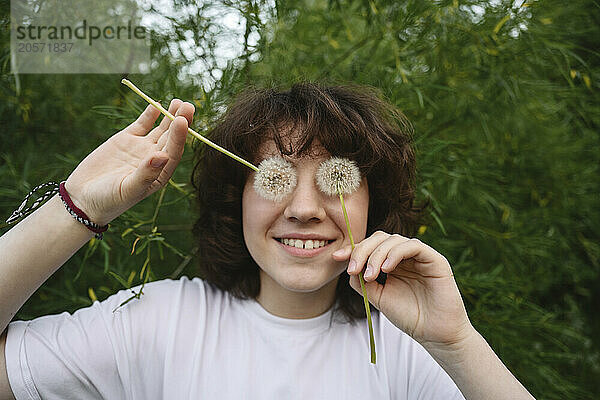 Smiling girl covering eyes with dandelions