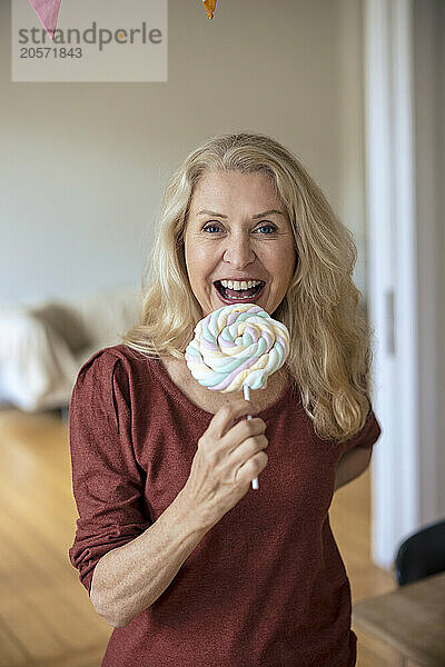 Cheerful blond woman eating lollipop at home