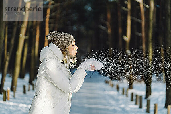 Woman blowing snow from hands in winter forest