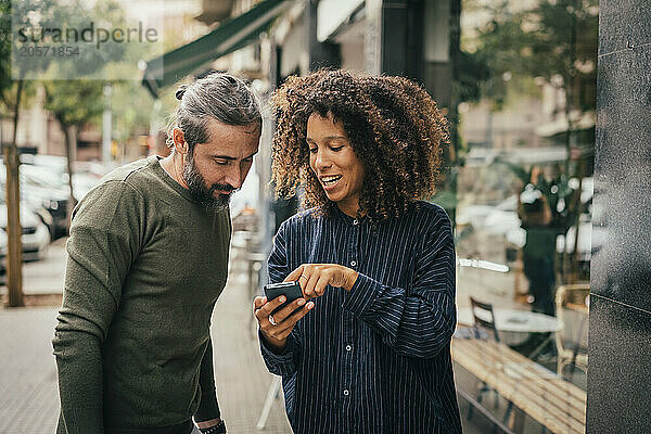 Young team members sharing smart phone near cafe