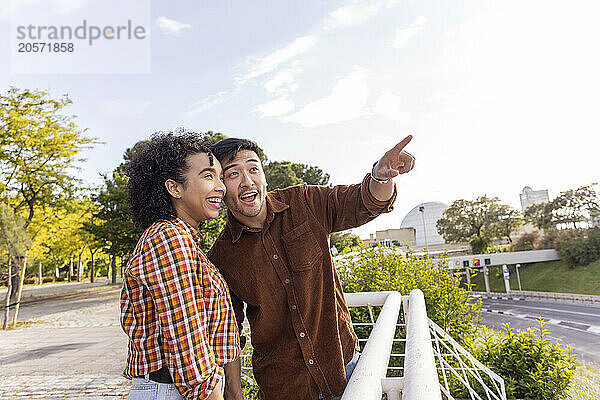 Excited man pointing at sky by girlfriend standing at park