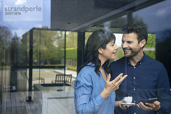 Happy businesswoman talking to businessman seen through glass window