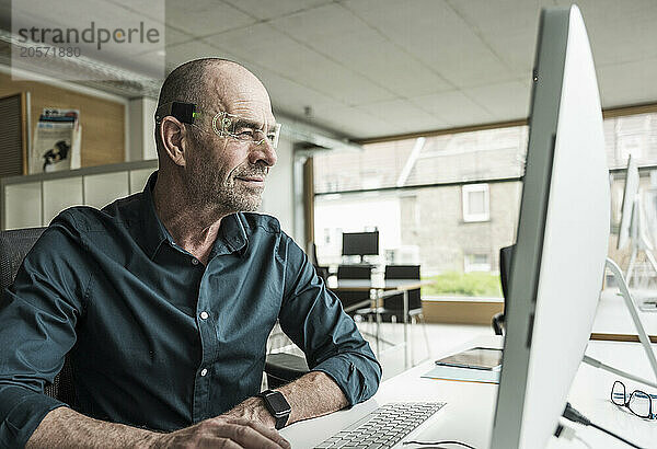 Smiling mature businessman wearing smart glasses using computer at workplace