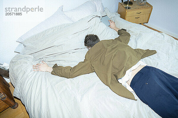 Young man lying on bed with arms outstretched at home