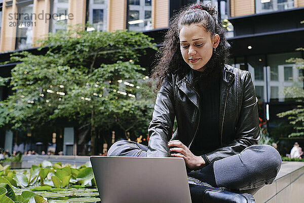 Young businesswoman sitting cross-legged using laptop in city