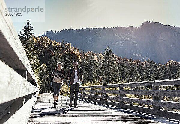 Mature couple with hiking poles on boardwalk at sunny day