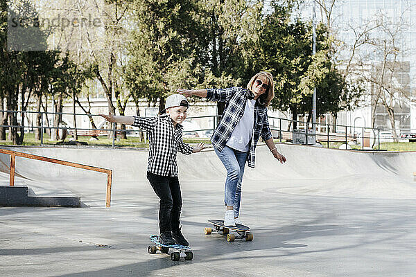 Smiling grandmother and grandson skateboarding on sports ramp in park