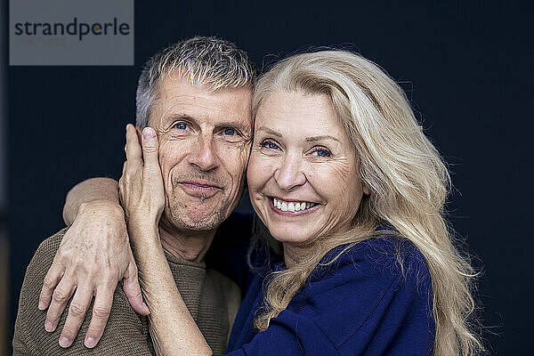 Cheerful blond senior woman with arm around man against black background