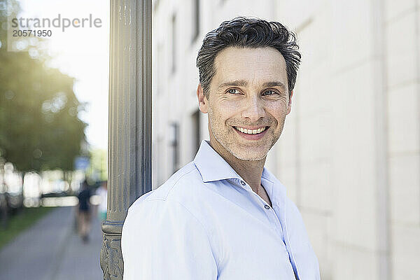 Smiling handsome mature businessman leaning on pole