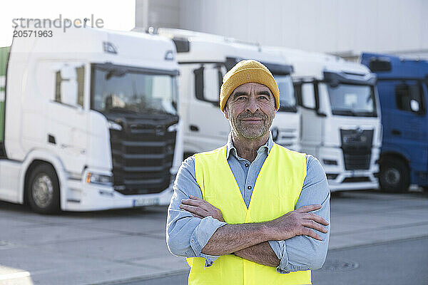 Smiling mature dock worker with arms crossed standing outside warehouse