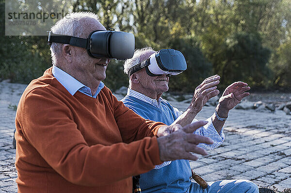 Friends using virtual reality glasses sitting at riverside