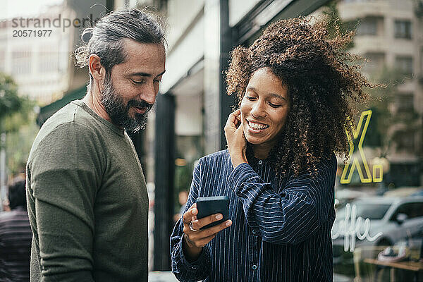 Young woman sharing smartphone with colleague outside cafe