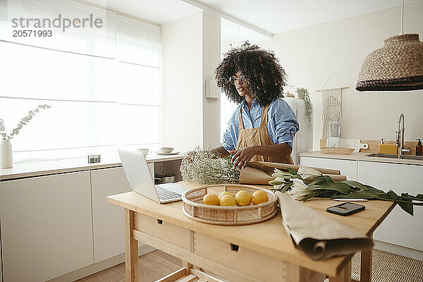 Woman with bouquet and laptop in kitchen