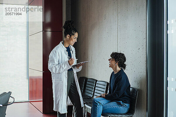 Happy doctor discussing with patient on chair in hospital