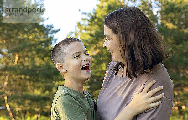 Happy mother and son laughing while standing in the park.