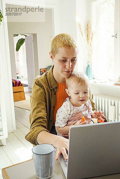 Blond freelancer using laptop sitting with daughter at home