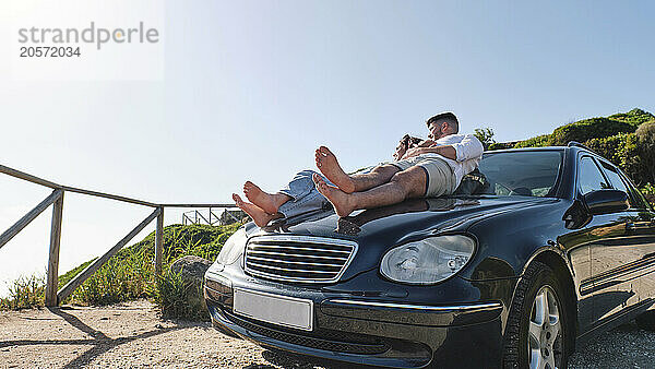 Boyfriend and girlfriend relaxing on car hood