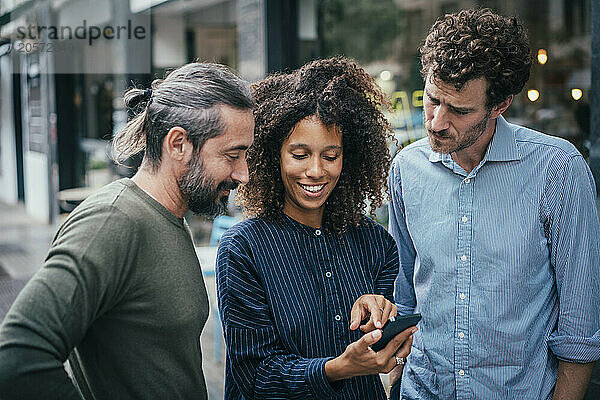 Business woman with blue shirt sharing smartphone with colleagues at street