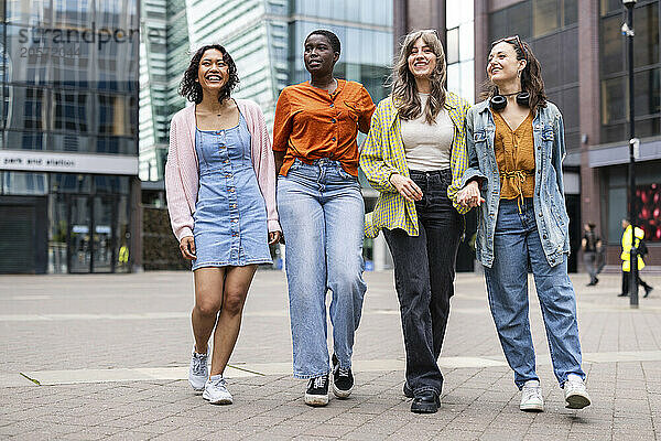 Smiling female friends walking on footpath in city