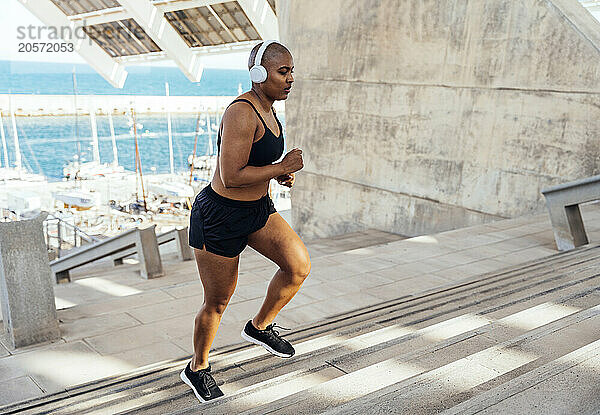 Sporty muscular woman wearing headphones jogging on stairs