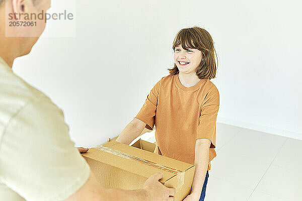 Happy daughter helping father carrying cardboard box in new house