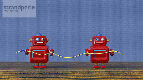 Small red robots with cable on table in front of blue textured wall