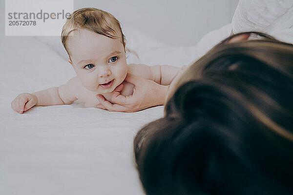 Cute baby boy lying on front with mother in bed at home