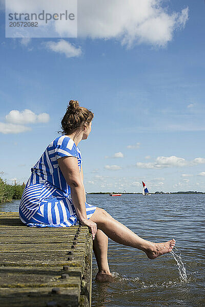 Mature woman sitting on pier of Friesland lake in Netherlands