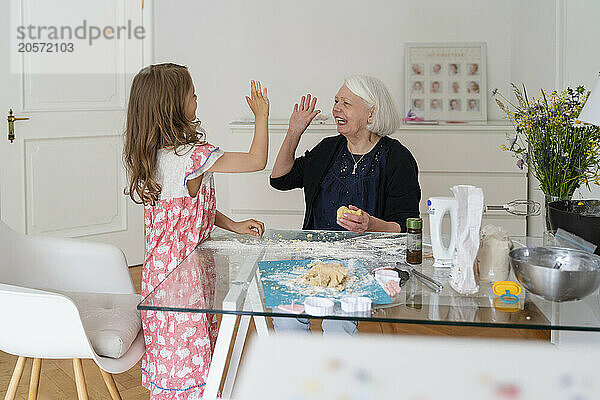 Happy grandmother and granddaughter giving high-five at home