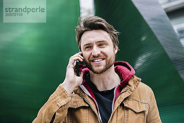 Handsome man talking on smart phone in front of green wall