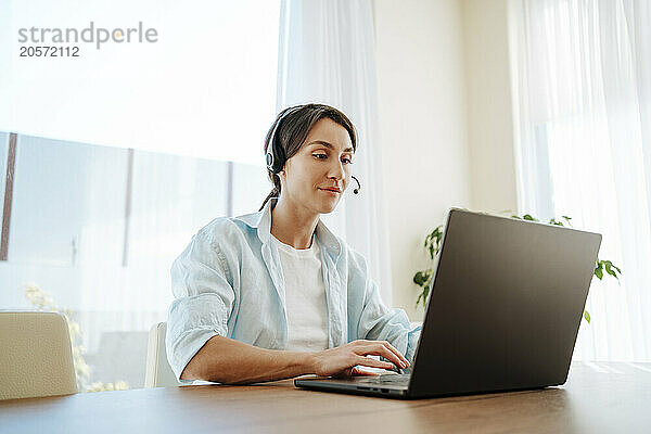 Confident businesswoman with headset using laptop at table working from home