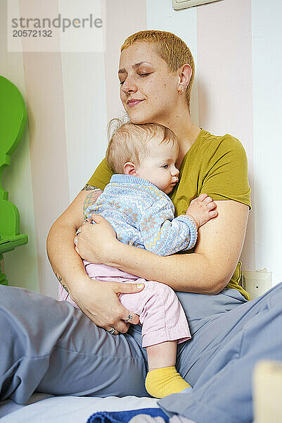 Woman with eyes closed taking care of toddler daughter sitting at home