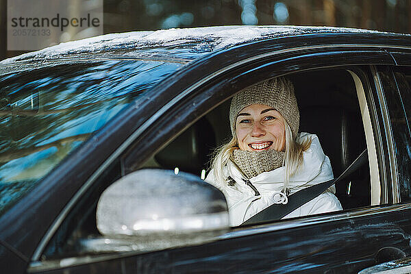 Happy woman wearing warm clothes and sitting in car