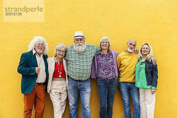 Happy fashionable elderly friends leaning on yellow wall