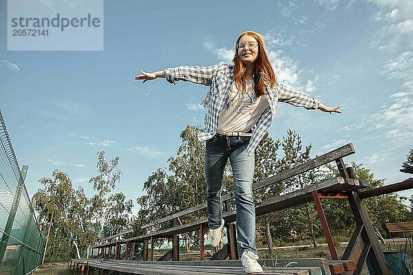 Playful girl with arms outstretched balancing on bench at public park