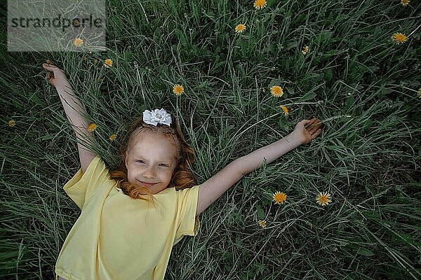 Girl with arms outstretched lying on grass in garden