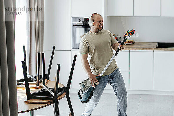 Man listening to music and imitating playing guitar with vacuum cleaner at home